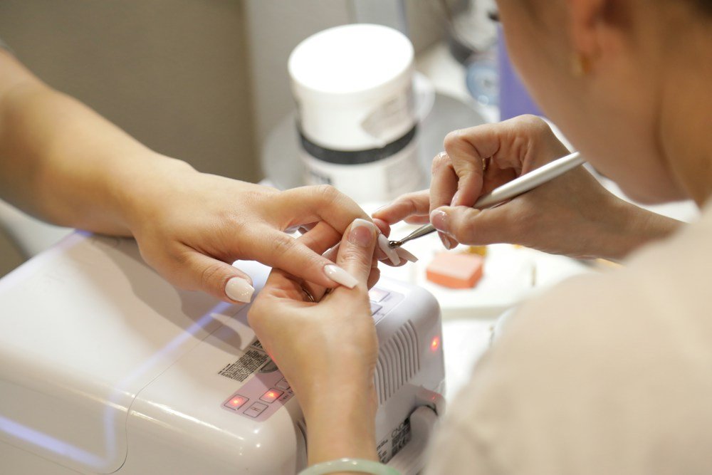 A technician working on a client's nails under a curing lamp